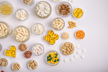 Nutritional supplements, minerals and vitamins in forms of colored pills, tablets and capsules in small jars on hite background from above. A large amount of vitamins.
