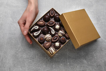 Woman with open box of delicious chocolate candies at light grey table, top view