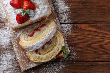 Pieces of delicious cake roll with strawberries and cream on wooden table, top view. Space for text