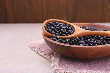 Fototapeta na wymiar Bowl and spoon of raw black beans on light grey table, closeup. Space for text