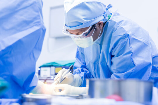 Doctor Or Surgeon In Blue Uniform Using Surgical Saw Inside Modern Operating Room In Hospital.Foot Amputation In Diabetic Foot Ulcer.People With Medical Glove And Mask.Asian Orthopedic Surgery.