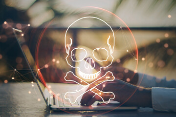 Close up of male hand using laptop and cellphone at desktop with digital red skull on blurry background. Ransomeware, virus and pirate threat concept. Double exposure.
