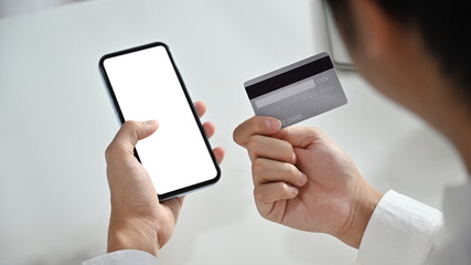 Cropped image of man hand holding credit card and using smartphone, making online transactions or shopping online
