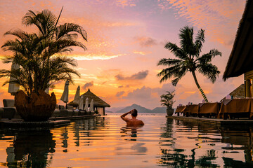 Luxury swimming pool in tropical resort, relaxing holidays in Seychelles islands. La Digue, Young man during sunset by swimpool