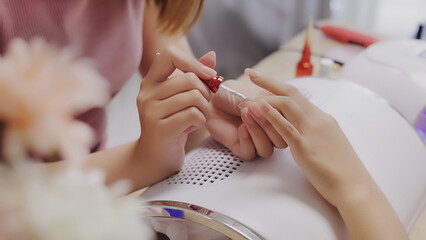 Close up Asian nail stylist apply color for a perfect polish nail to customer. Manicure concept....