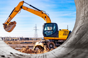 Wheeled works in a pit at a construction site. The excavator carries out excavation work on the background of a cloudy sky. View from the trench. Preparation of a pit for construction.