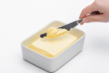 Kostka bloczek masła w białej maselniczce i dłoń z nożem zeskrobująca kawałki na kanapkę makro 