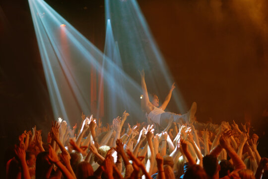 Stage dive, hands and people at music festival, neon spotlight and energy at live concert event. Dance, fun and group of excited fans in arena at rock show performance, audience carrying crowd surfer