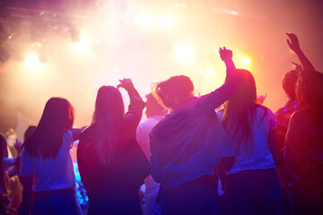 Crowd, people dancing at concert or music festival from back, neon lights and energy at live event. Dance, fun and group of excited fans in arena at rock band performance or audience at rave party.