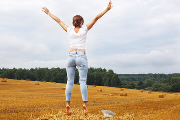 Fototapeta premium girl with straw hat stands on a haystack on a bale in the agricultural field after harvesting