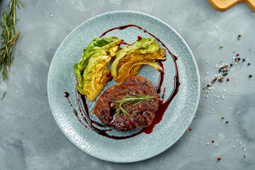 Grilled beef steak with a side dish of cabbage and sauce in a plate on a gray background
