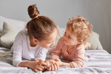 Playful children. Happy childhood. Lazy morning. Cute little girls playing in bedroom lying in bed siblings spending time together.