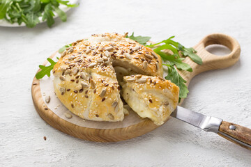 Baked in puff pastry cheese sprinkled with seeds decorated with fresh arugula leaves on a wooden board on a gray textured background