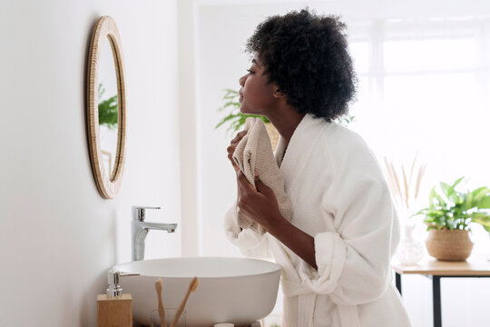 Young woman wiping face with towel looking in mirror at home
