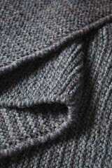 Dark gray knitted fabric folded in a zigzag pattern. Knitted texture background.