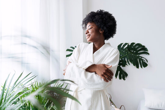 Smiling woman hugging self standing near plants at home
