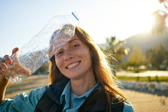 Smiling volunteer holding plastic bottle near forehead at beach