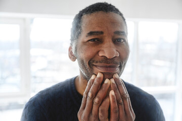 Smiling mature man with hand on chin at home