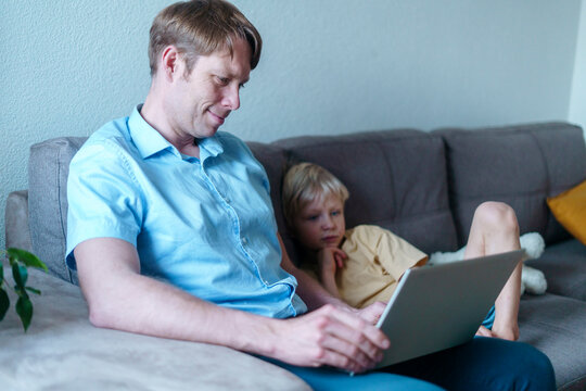 Smiling father working on laptop with son sitting in living room at home