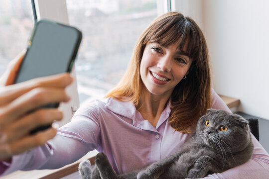 Happy woman taking selfie with cat through smart phone