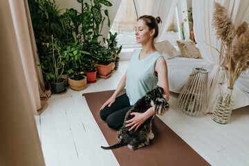 Woman practicing meditation with Schnauzer dog on exercise mat at home