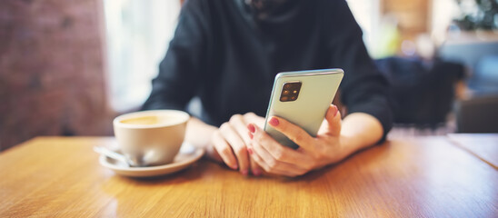 Woman holding phone in her hands and sitting in cafe at the table with cup of coffee.
