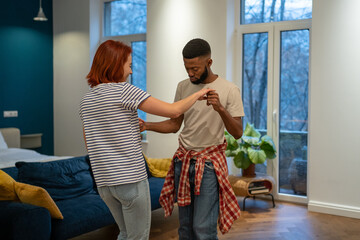 Young diverse couple in love preparing first wedding dance together, black man and caucasian girl dancing in living room, African guy teaching girlfriend how to dance during home date night