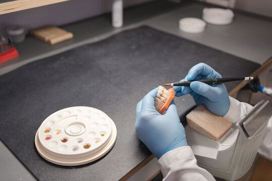 Technician dental is working with complete lower and upper metal ceramic prosthesis dental. Dental technician works by brush with jaw model