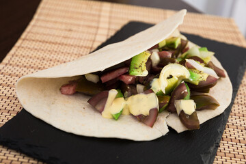 salad of black tomatoes, avocado and onions in Italian tortilla on black stone board