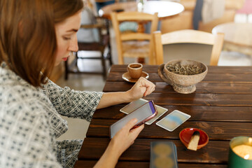 Beautiful young woman is guessing on cards with tarot, runes on wooden table and uses an online app in phone to interpret divination, home interior,candles and dry herbs..