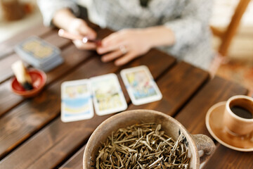 Fortune teller with tarot cards on table near burning candle.Tarot cards spread on table with magic herbs and palo santo aroma sticks. Forecasting concept