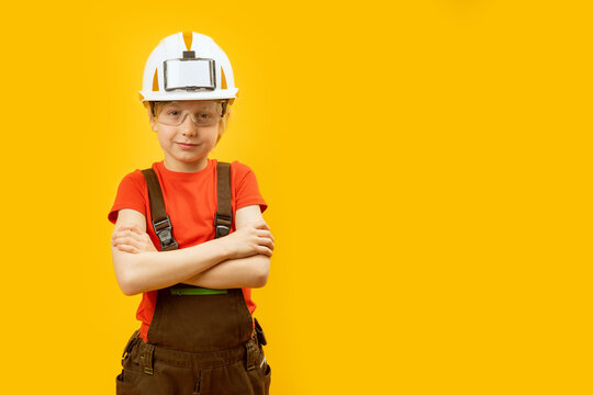 Portrait of boy in work overalls, protective helmet and glasses on yellow background. Choosing profession concept. Copy space.