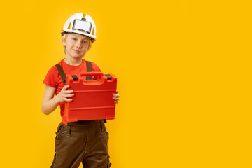 Portrait of blond boy in white protective helmet with box for instruments is insulated on yellow background. Copy space, mockup
