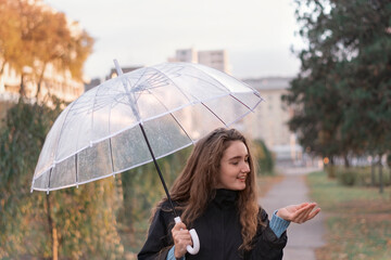 Young woman with long brown hair standing with umbrella in park. Girl with an umbrella on cloudy autumn day.