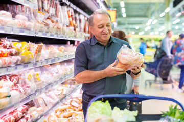 Mature man choosing packaged piece of meat in grocery store