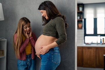 Curious excited little girl looking at mother's stomach. Beautiful pregnant single mother with her adorable young daughter at home.