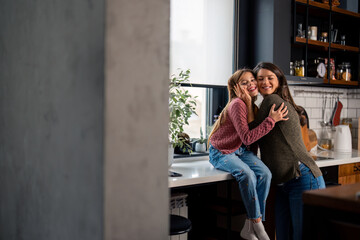 Affectionate pregnant mother and her young daughter embracing in kitchen at home. Family, childhood, love, pregnancy and support.