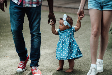 Portrait of candid happy interracial family walking with swarthy baby holding hands at camper park