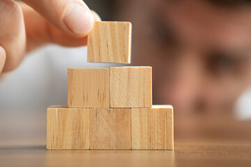 Close-up photo of putting wooden block on top of pyramid. Thinking about next step. Planning business growth. Horizontal concept with copy space for your text.