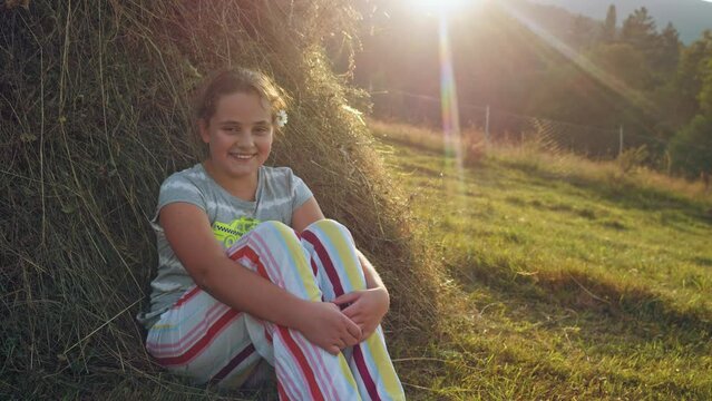 Kid girl sitting near the hay on sunset background