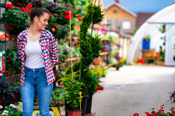 a flower girl poses next to her plants in front of a greenhouse
