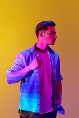 Handsome young man in casual stylish clothes posing with serious expression over yellow background with gradient neon lights. Concept of modern photography, art, cyberpunk, techno, creativity, fashion