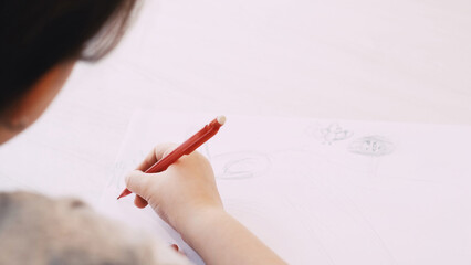 Creative picture. Kids painting. Art hobby. Unrecognizable child drawing on white paper with pencil sitting table blurred.
