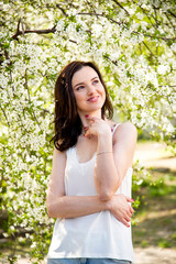 portrait of smiling happy brunette beautiful woman in white T-shirt and pink manicure with white cherry blossoming in the spring sunny day 