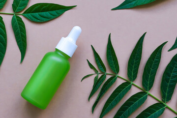 Green glass dropper bottle with natural green leaves on a beige background. Natural, organic cosmetics.
