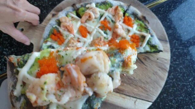 Eating spliting seafood shrimp pesto wasbi fusion pizza cheese on wood board top view POV slow motion video