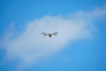 a drone with a high-resolution digital camera flies against a blue sky with clouds, a drone hovers in the air against the sky, a copter hovers in the air