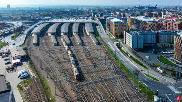 Train leaving main railway station in Krakow, Poland. Big parking lot on the roof, roofed platforms, cars and electric traction. Old town with main monuments in the background. Aerial view