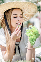 A young farmer woman eats white grapes picked by herself at the green grapes vineyard. Picnic in the blooming garden