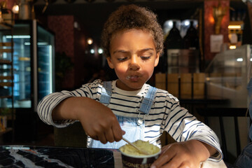Portrait of African American boy eating ice cream in a restaurant.